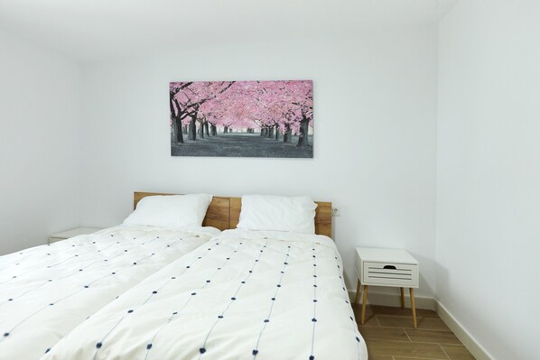 A bedroom with a bed, white bedding, a small bedside table, and a wall-mounted picture of cherry blossoms.
