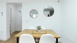 Un coin repas avec une table en bois, des chaises blanches, deux miroirs ronds et une petite plante en pot.