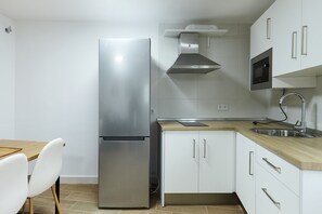 A modern kitchen with a stainless steel refrigerator, wooden countertop, white cabinets, and a built-in microwave.