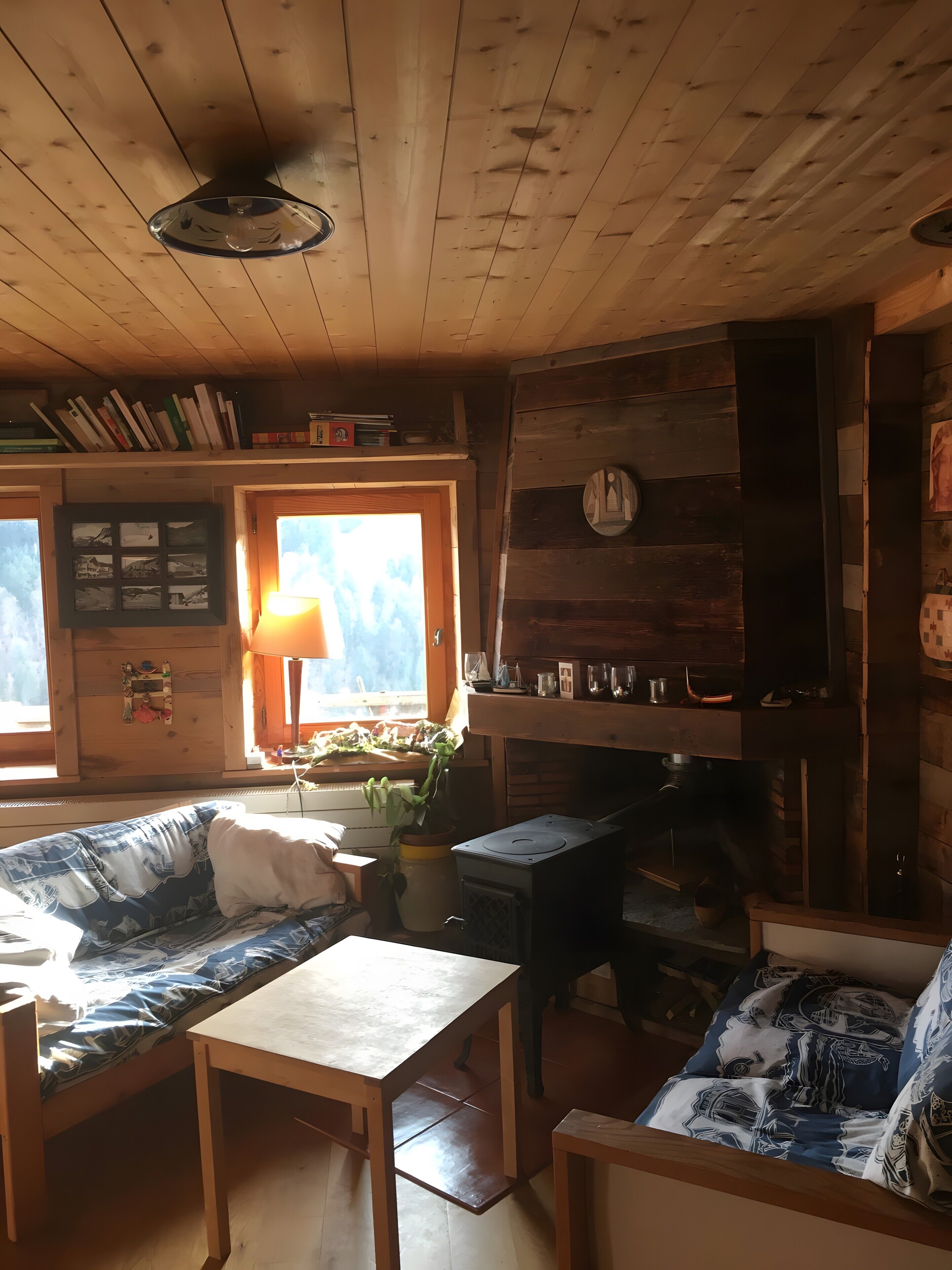 Ein gemütliches Blockhaus-Interieur mit Holzbalkendecke, einer Couch, einem Tisch, einem Kamin und einem Fenster mit Aussicht.