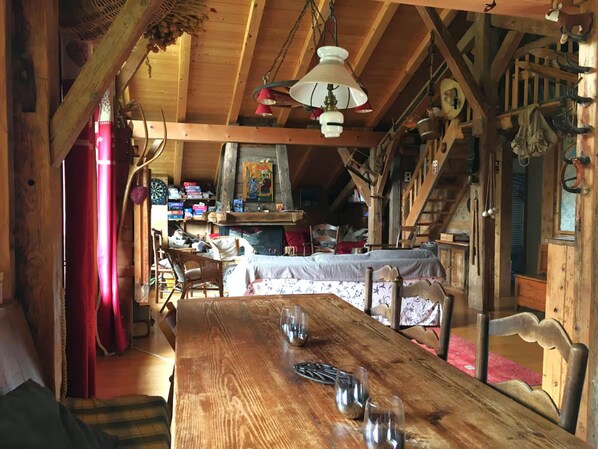 A rustic wooden interior with a wooden table, chairs, a bed, and a fireplace.