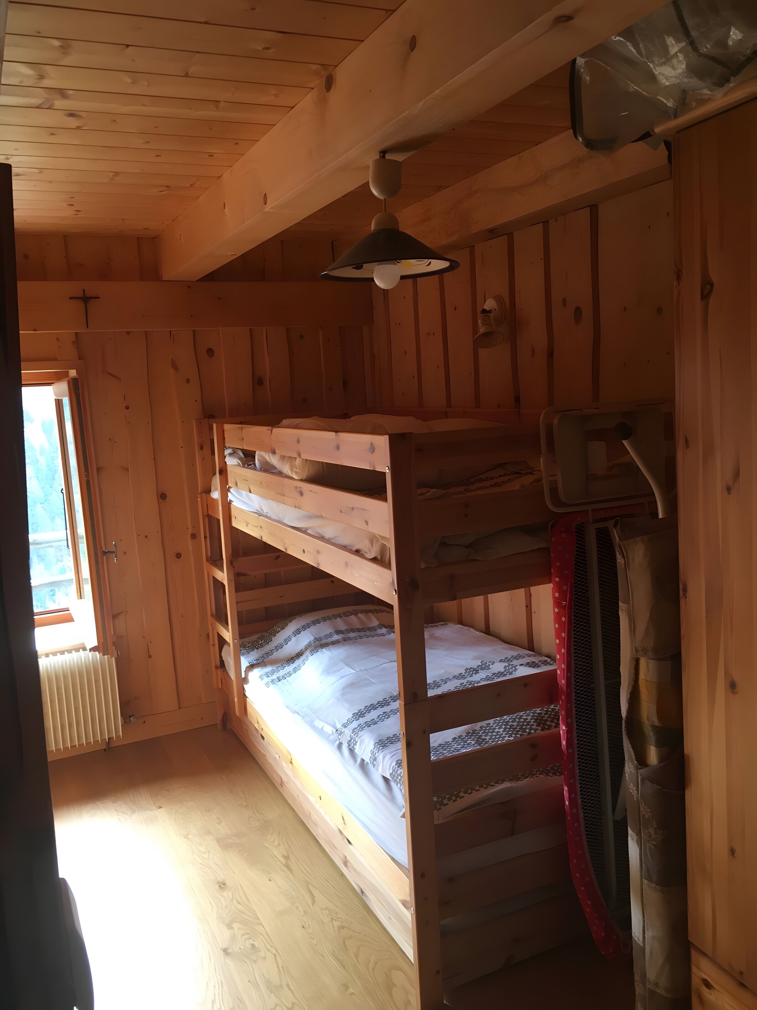 Une cabane en bois avec des lits superposés, un radiateur et un luminaire au plafond.