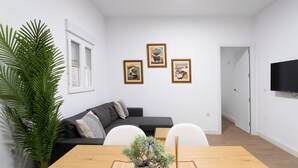 Un salon moderne avec un canapé, une table à manger agrémentée d’un bonsaï et trois œuvres d’art encadrées accrochées au mur.