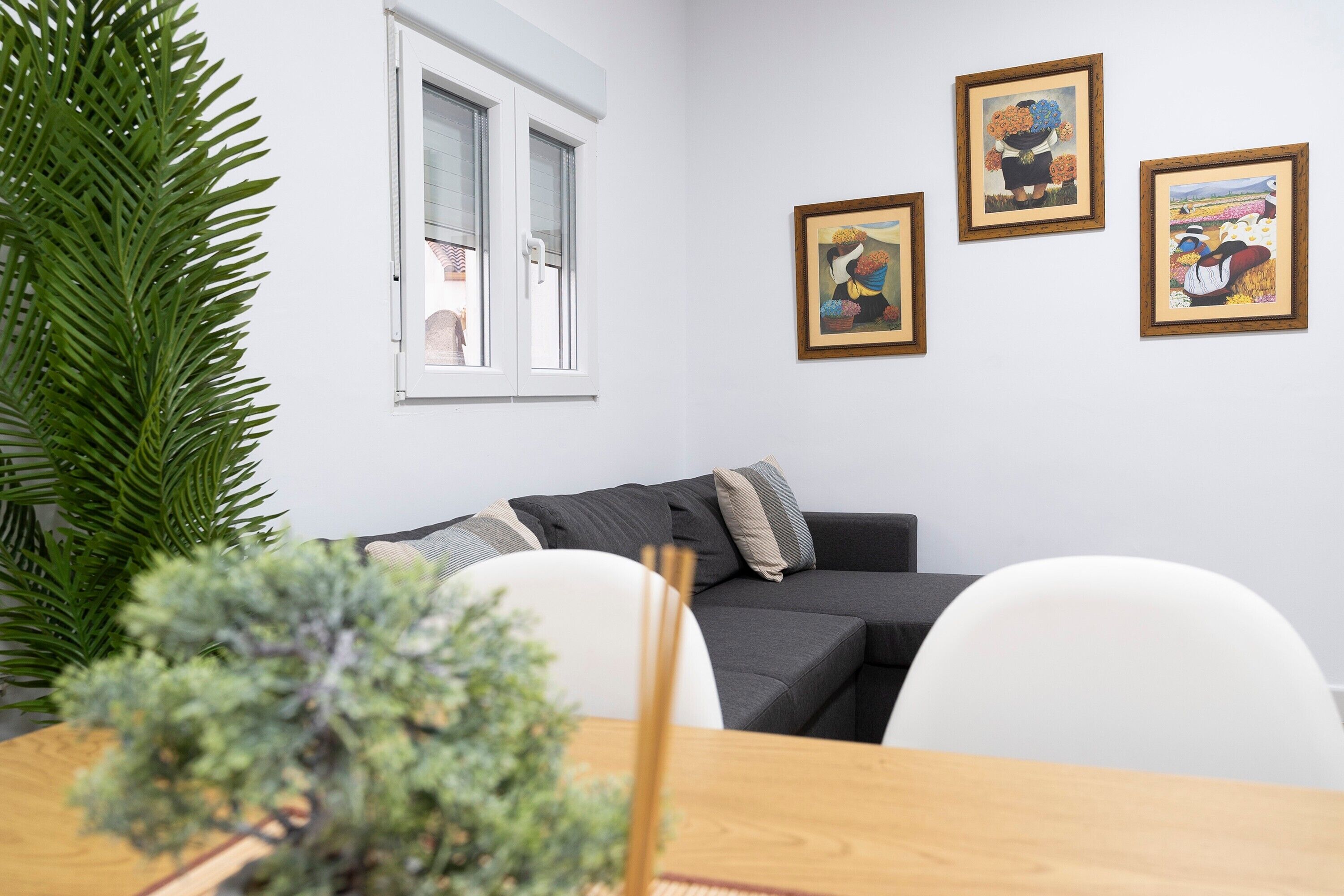 Un salon moderne avec un canapé gris, des chaises blanches, une table à manger en bois et des œuvres d’art encadrées accrochées au mur.