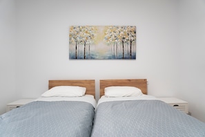 Un dormitorio con dos camas, un cabecero de madera, una mesita de noche y un cuadro con árboles en la pared.