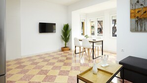 Ein modernes Wohnzimmer mit Schachbrettfußboden, einem Flachbildfernseher, einem Essbereich mit Stühlen und einem großen Fenster.