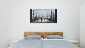 Ein Bett mit einem hölzernen Kopfteil, zwei Nachttische und ein an der Wand hängendes Bild einer Straßenszene.