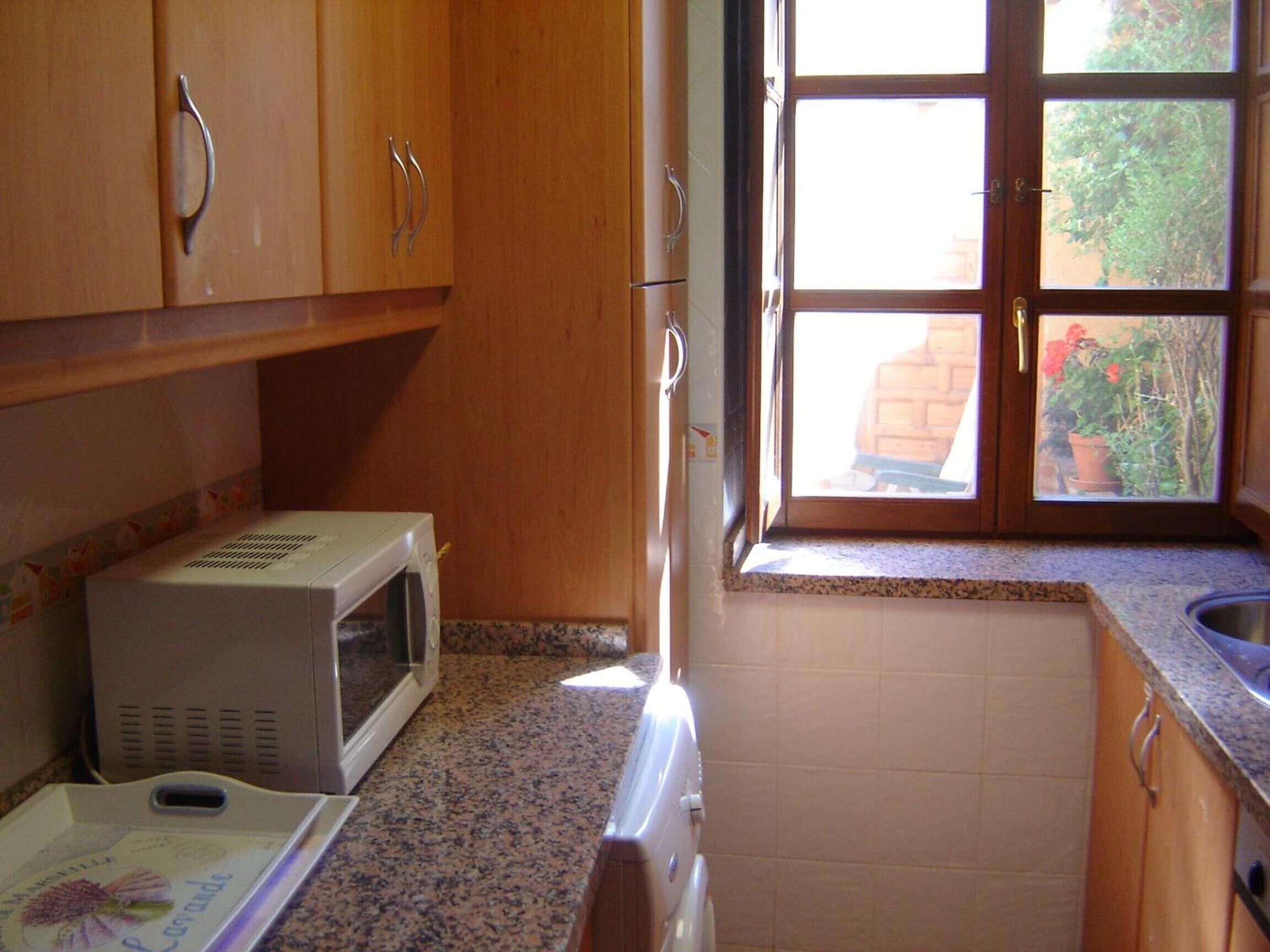 A kitchen with wooden cabinets, a microwave, a window with a view of greenery, and a granite countertop.