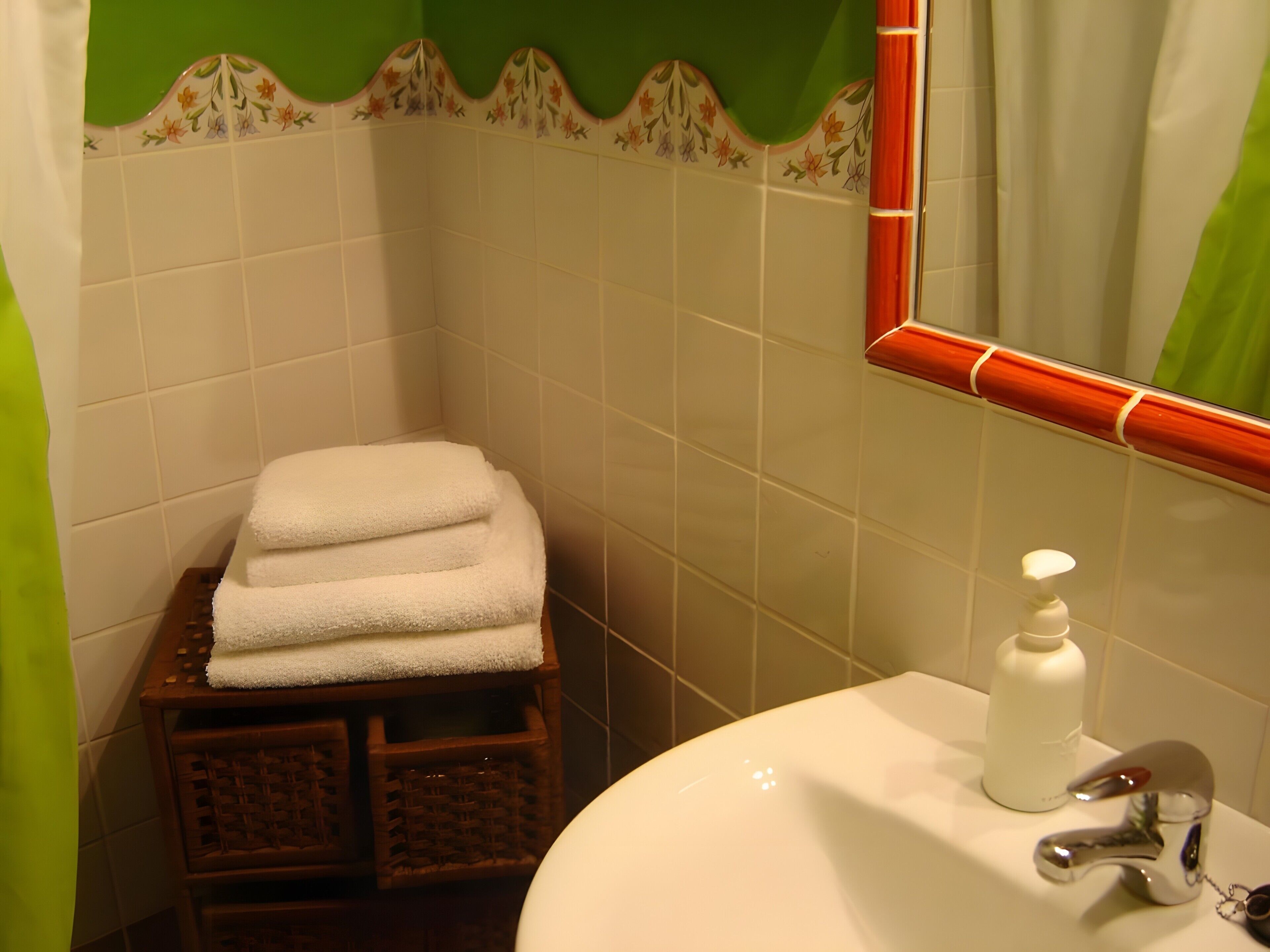 Un baño con un lavamanos, un espejo y una pila de toallas blancas sobre un taburete de madera.