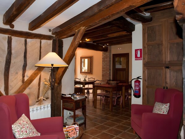 A cozy room with exposed wooden beams, a dining area with a table and chairs, and a red sofa with floral cushions.