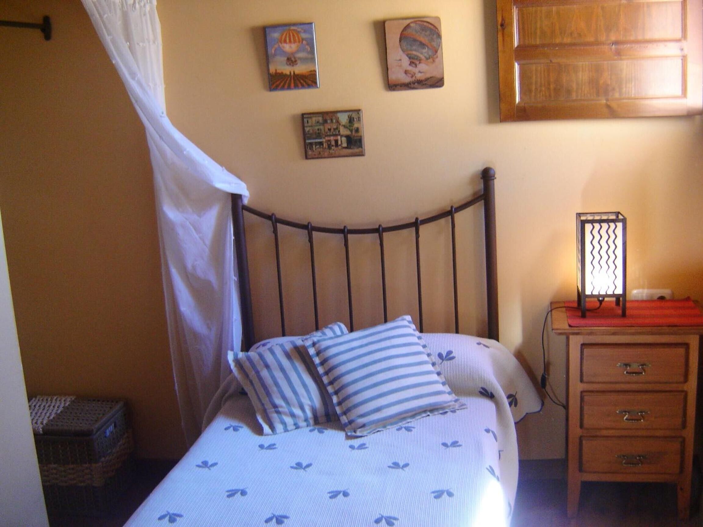 Ein Bett mit Metallkopfteil, ein Nachttisch mit Schubladen, eine Wandlampe und zwei gerahmte Bilder.