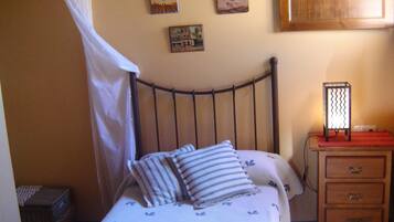 Ein Bett mit Metallkopfteil, ein Nachttisch mit Schubladen, eine Wandlampe und zwei gerahmte Bilder.