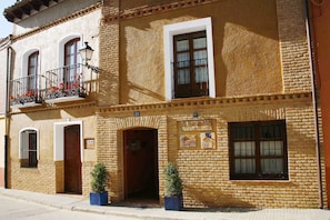 A two-story building with a brick facade, a balcony with red flowers, and a sign indicating it is a hotel.