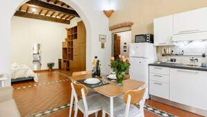 A dining area with a table set for two, a kitchen with white cabinets, and a wooden bookshelf.