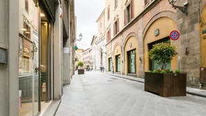 A narrow street with buildings on either side, a no parking sign, and a planter with a tree.