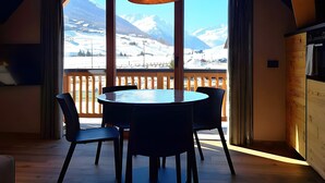 A dining area with a table and chairs, a hanging light fixture, and a view of snow-covered mountains through large windows. - Apartment 'Livigno' with Mountain View, Private Terrace and Wi-Fi (Livigno)