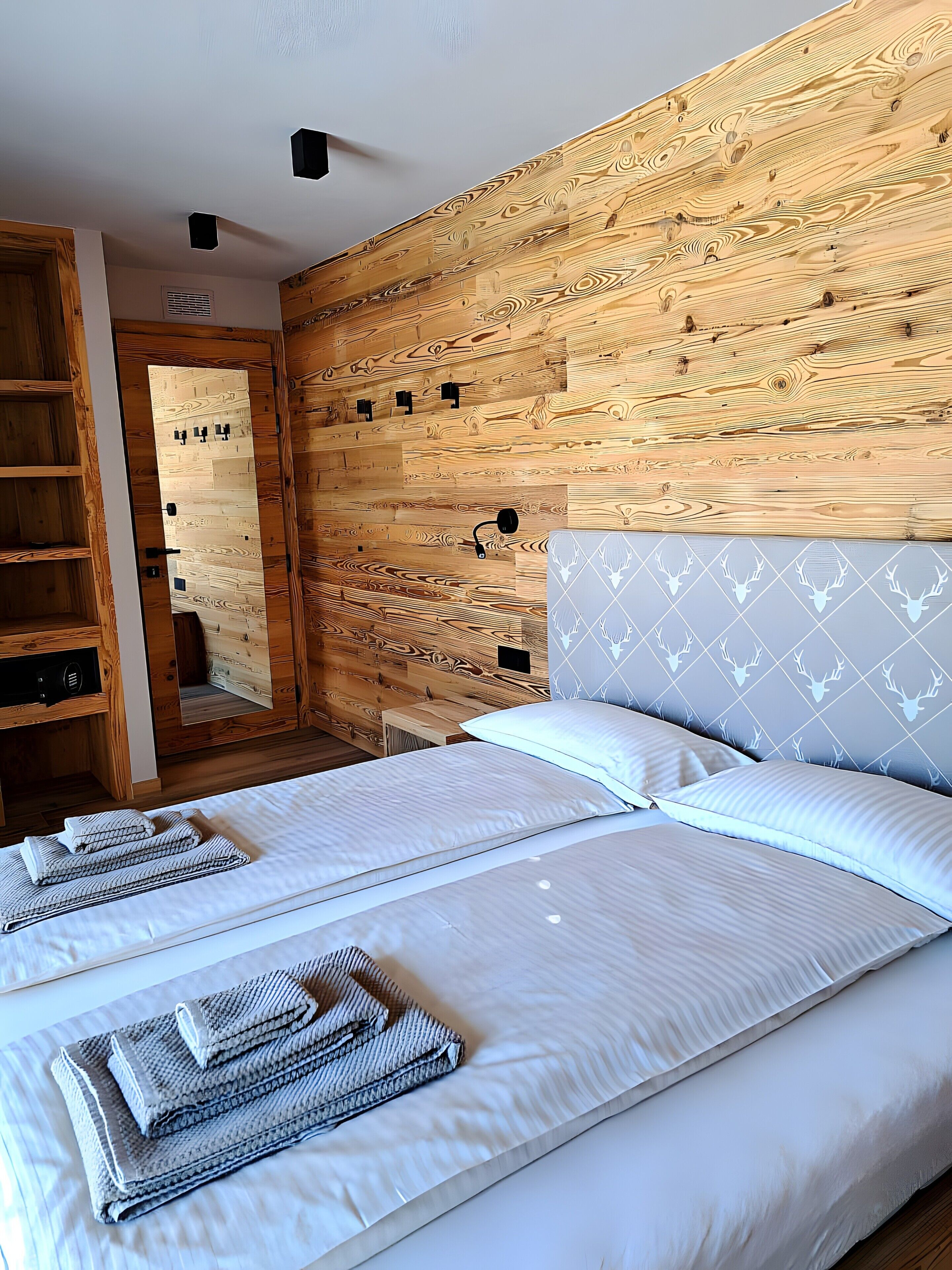 A bedroom with a wooden headboard, two beds with white linens, and a wooden wardrobe.