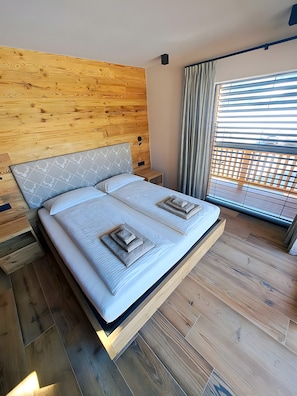 A bed with a headboard, a bedside table, and a window with blinds. - Apartment 'Livigno' with Mountain View, Private Terrace and Wi-Fi (Livigno)