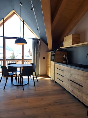 A modern kitchen with wooden cabinets and a dining area with a round table and chairs. - Apartment 'Livigno' with Mountain View, Private Terrace and Wi-Fi (Livigno)