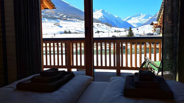 A room with two beds, a view of snow-covered mountains, and a wooden balcony. - Apartment 'Livigno' with Mountain View, Private Terrace and Wi-Fi (Livigno)