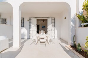 Un intérieur aux couleurs claires, avec une table à manger et des chaises, un ventilateur de plafond et un téléviseur en arrière-plan.