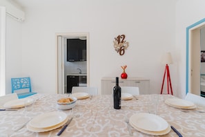 A dining area with a table set for four, a wine bottle, and a bowl of food.