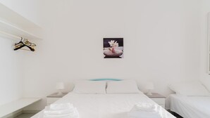 Una habitación de hotel con una cama, dos mesitas de noche, un cuadro en la pared y un perchero.