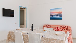 Un comedor con una mesa preparada para cuatro personas, una botella de vino y un sofá con funda estampada en rojo y blanco.