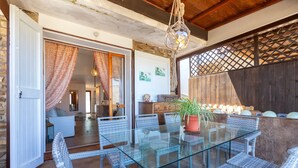 An open dining area with wicker chairs and a glass table, a wooden ceiling, and a view into a living room. - Holiday Home 'Jacuzzi' with Sea View, Wi-Fi and Air Conditioning (Stintino)