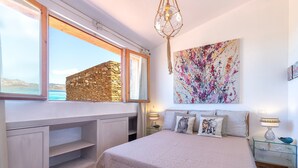 A bedroom with a stone wall, a bed with a quilt, a nightstand, a lamp, and a painting. - Holiday Home 'Jacuzzi' with Sea View, Wi-Fi and Air Conditioning (Stintino)