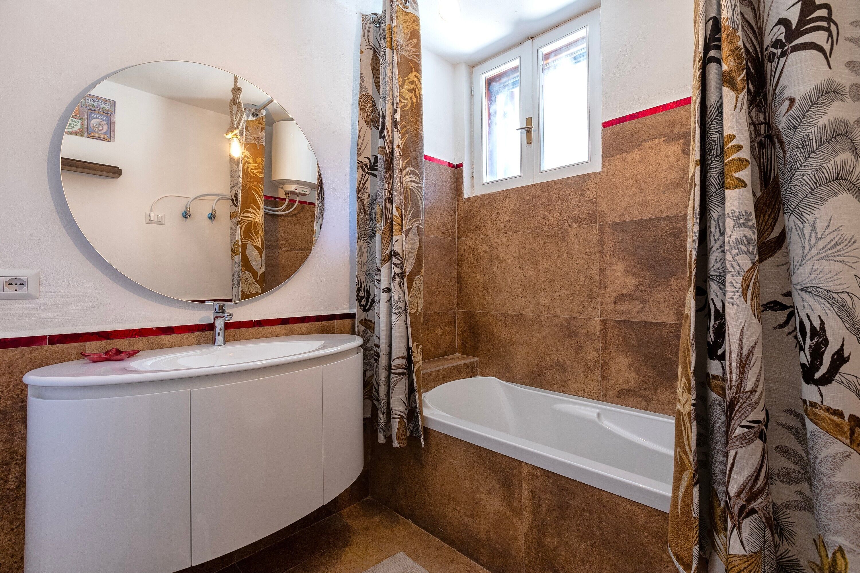 Een badkamer met een ronde spiegel, een wastafel, een badkuip en gordijnen met een patroon.