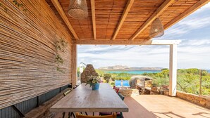 An outdoor dining area with a wooden table and chairs, a stone wall, and a view of the sea and mountains. - Holiday Home 'Asinara' with Sea View, Wi-Fi and Air Conditioning (Stintino)