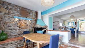 A stone wall, a wooden table with blue chairs, and a kitchen area with a blue accent wall. - Holiday Home 'Asinara' with Sea View, Wi-Fi and Air Conditioning (Stintino)