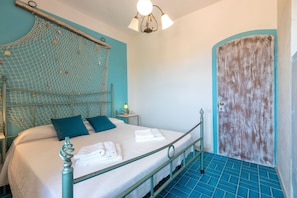 Una habitación con una cama, un cabecero con mosquitera, una puerta y un piso de azulejos azules.