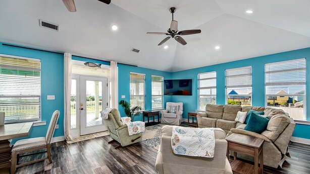 A spacious living room with a ceiling fan, large windows with blinds, a wooden floor, and a view of the outside. - Coastal View: Beach/Fishing/ Coastal Realty Group (Grand Isle)