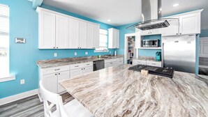 A modern kitchen with white cabinets, a marble countertop, stainless steel appliances, and a blue accent wall. - Coastal View: Beach/Fishing/ Coastal Realty Group (Grand Isle)