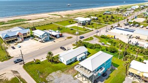 An aerial view of a coastal area with a beach, a road, and several buildings including a large blue structure with a deck. - Coastal View: Beach/Fishing/ Coastal Realty Group (Grand Isle)
