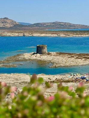 Un paysage côtier caractérisé par une imposante tour de pierre, un terrain rocheux et une plage parsemée de parasols.
