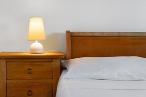 Ein Nachttisch aus Holz mit Lampe und Schublade neben einem Bett mit weißer Bettwäsche.