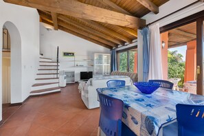 A spacious living area with a high ceiling, a dining table with chairs, a sofa, and a television.