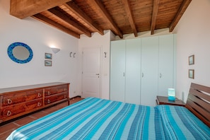 Um quarto com cama, cómoda de madeira, guarda-roupa e espelho na parede.