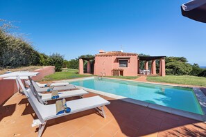 A swimming pool with lounge chairs and a small building with a tiled roof.