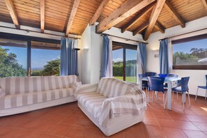 A room with a wooden ceiling, a striped sofa, a dining table with chairs, and large windows with curtains.