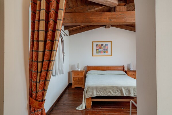 A bedroom with a wooden bed, a nightstand, a framed picture on the wall, and a wooden ceiling.