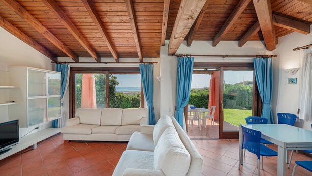 A spacious living area with a wooden ceiling, a white sofa, a TV, and a dining table with blue chairs. - Villa 'Alba Piscina Vista Mare' with Sea View, Wi-Fi and Air Conditioning (Stintino)