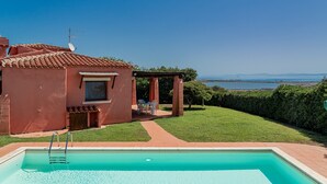 A swimming pool with a view of the sea, a red building, and a patio area. - Villa 'Alba Piscina Vista Mare' with Sea View, Wi-Fi and Air Conditioning (Stintino)