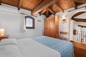 A bedroom with a bed, a wardrobe, a chair, a window with curtains, and a wooden ceiling.
