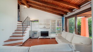 A living room with a staircase, a flat-screen TV, white sofas, and a bookshelf. - Villa 'Alba Piscina Vista Mare' with Sea View, Wi-Fi and Air Conditioning (Stintino)