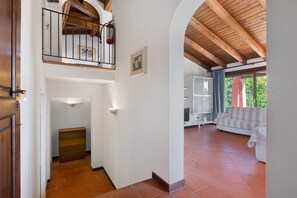 A spacious living area with a high ceiling, a staircase leading to an upper floor, and a view of greenery outside.
