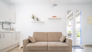 Un salon aux couleurs neutres, avec un canapé beige, des meubles blancs et une porte vitrée donnant sur un espace extérieur.